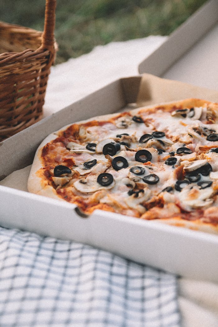 Tasty pizza with cheese, olives, and mushrooms in a cardboard box for outdoor picnic.